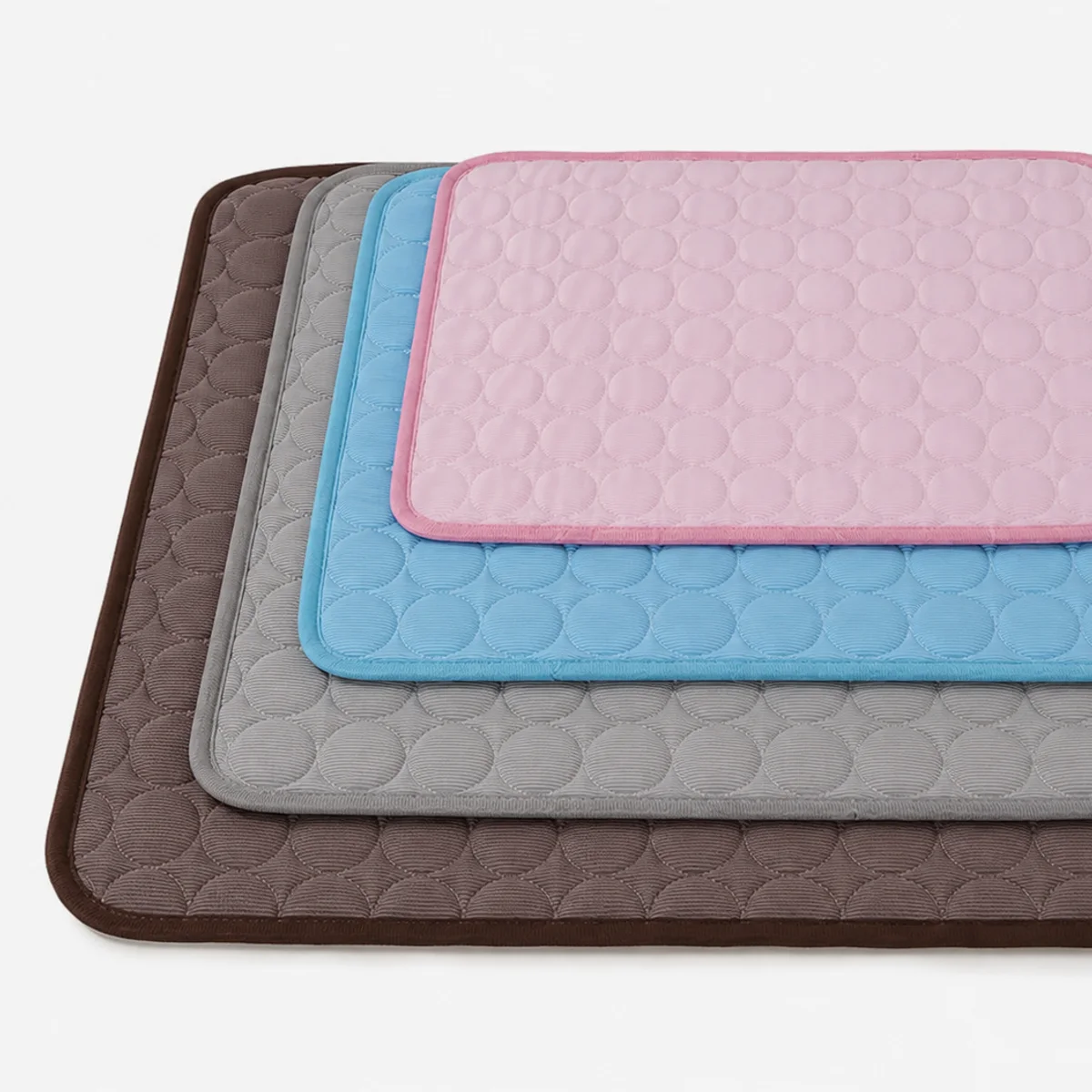 Os quatro tapetes gelados Frimouf empilhados por tamanho: P rosa, M azul, G cinza e GG marrom